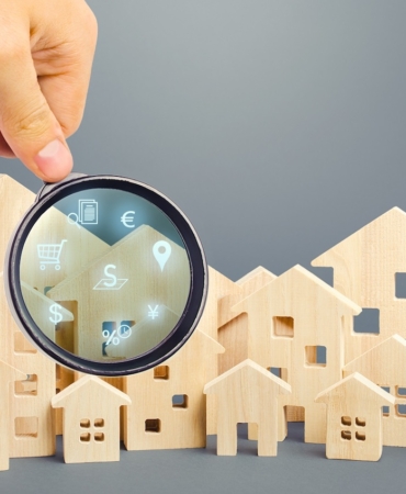 Realtor examines houses through a magnifying glass. Review of the real estate market, search for the best offers based on the criteria of price, location, area, infrastructure. Customer preferences.